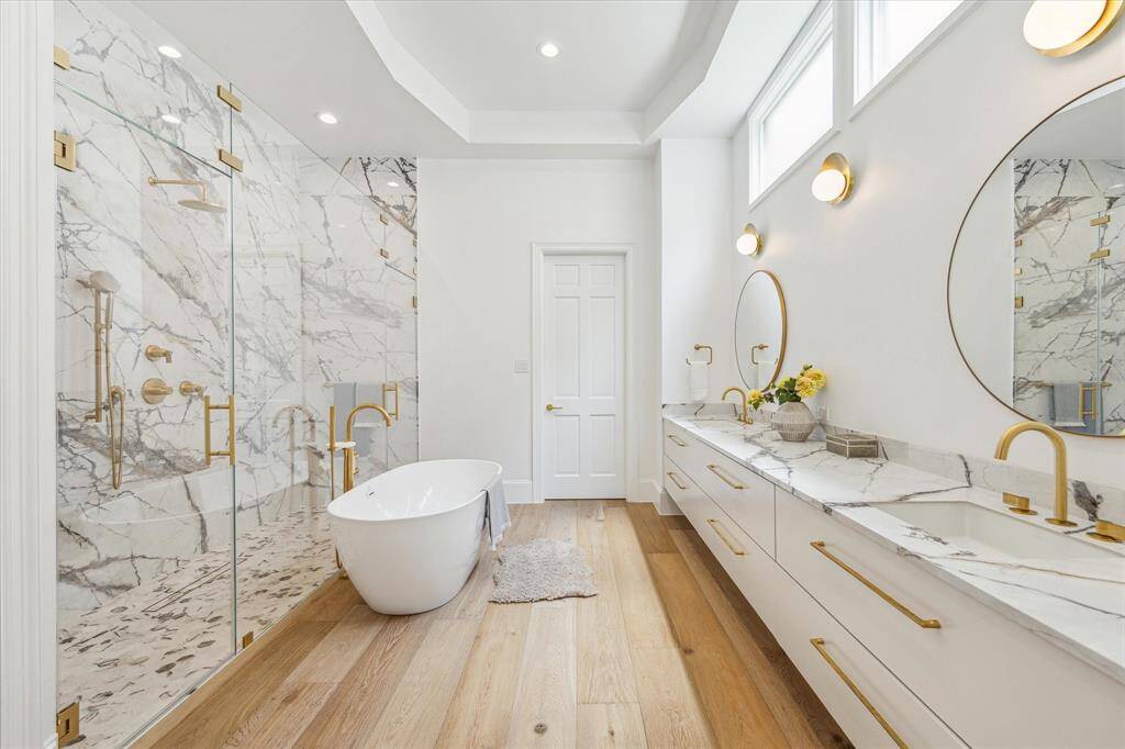 A true spa experience—this primary bath showcases floor-to-ceiling marble, dual vanities, brass hardware, and a freestanding soaking tub.