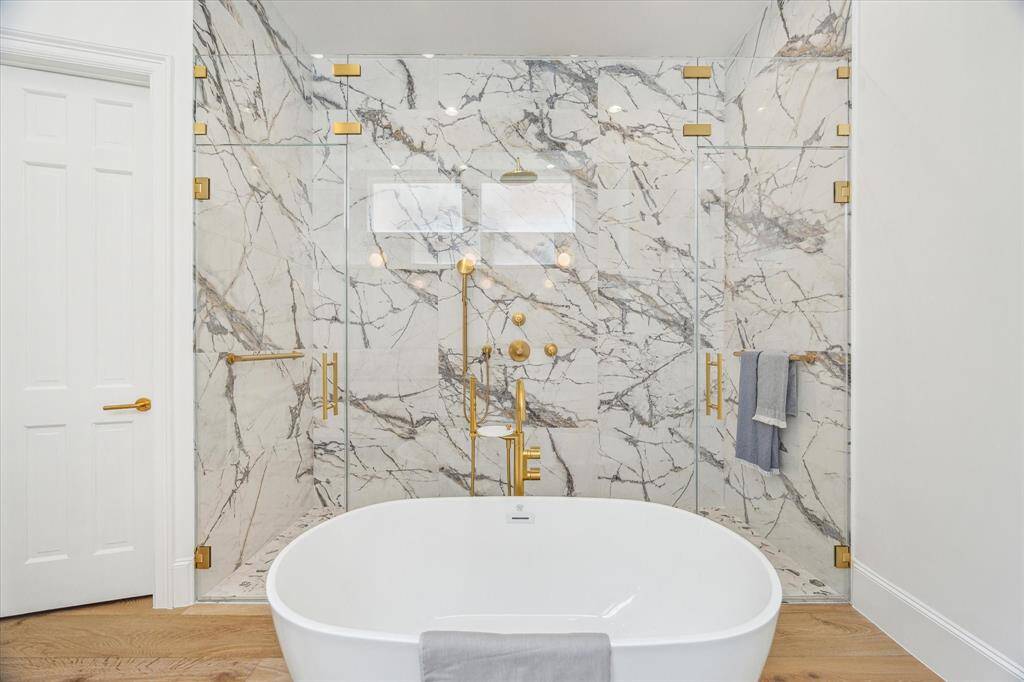 An oversized frameless glass shower takes center stage alongside a sculptural soaking tub, both set against a stunning backdrop of marble.