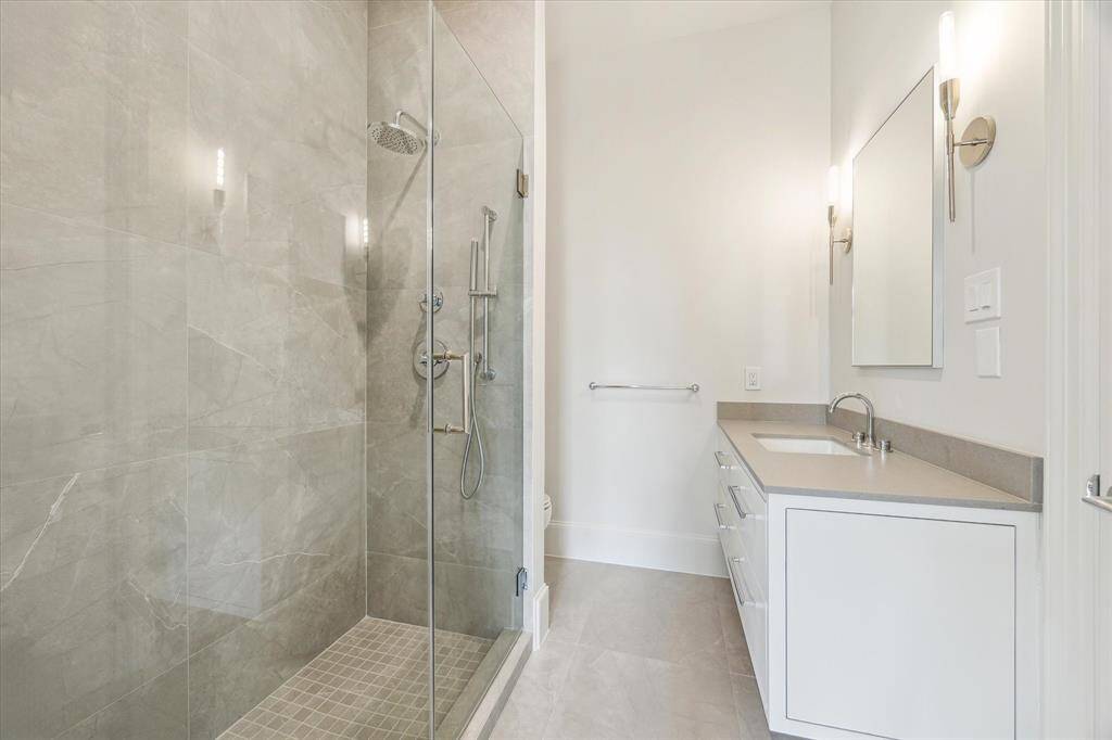 Secondary bathroom with a spacious frameless glass shower, contemporary sconces, and a clean, calming palette that exudes understated luxury.