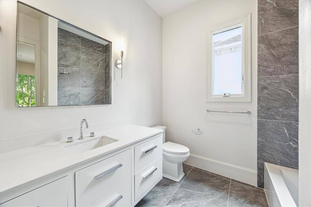 This secondary bath features tile floors, sconce and recessed lighting, a large vanity with ample storage, and tub/shower combo, and natural light for a refreshing retreat.