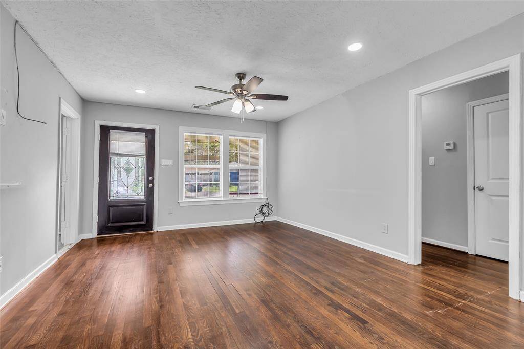 The living room features large glass windows with a view of the front lawn. To the left, a hallway leads to the secondary bedrooms and the shared bathroom, providing a practical layout for everyday living.