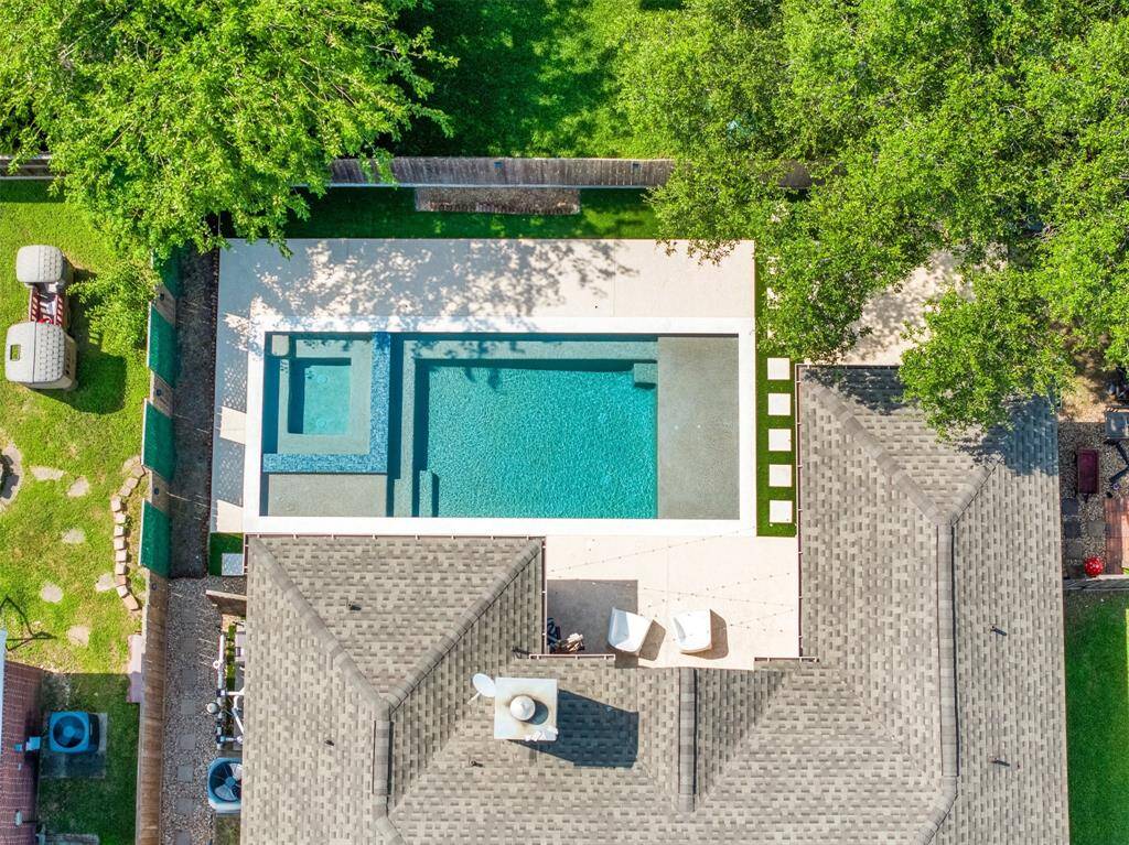 This aerial photo showcases a modern backyard featuring a sleek rectangular pool with an attached spa. The area is surrounded by well-maintained greenery and has ample patio space for relaxation and entertainment. The layout provides a private and inviting outdoor oasis.