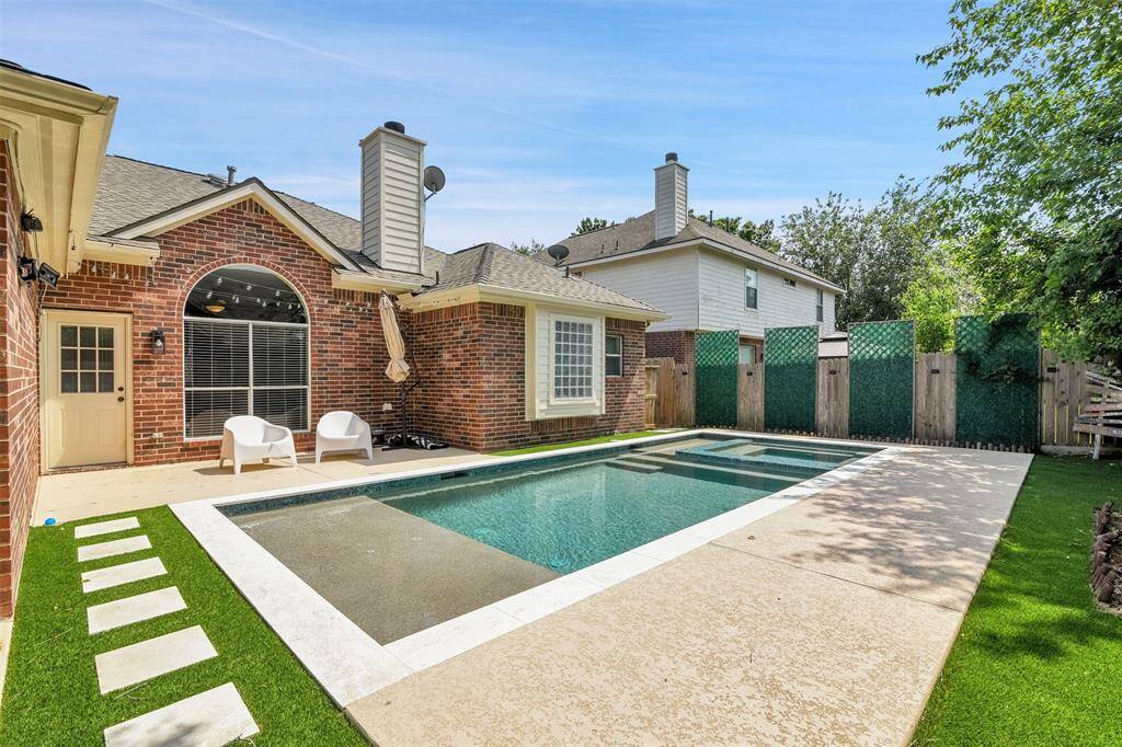 This photo showcases a charming backyard with a brick exterior, featuring a well-maintained pool and cozy seating area under string lights. Perfect for relaxing and entertaining.
