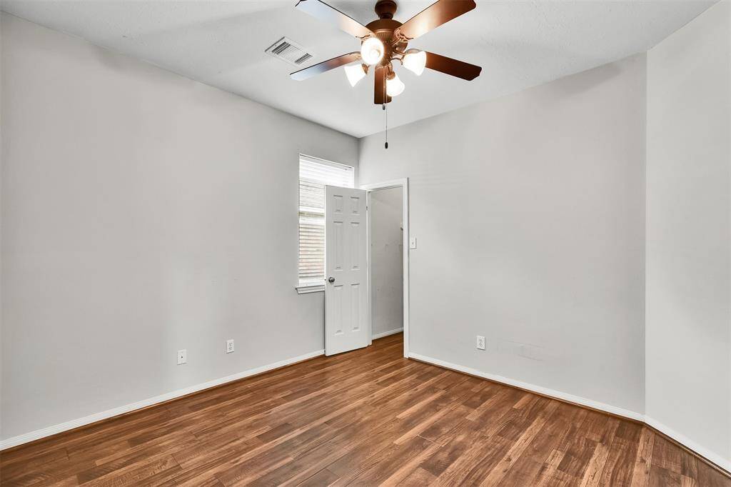 This room features laminate flooring, a ceiling fan with lights, and a mounted TV on the wall. It has a tray ceiling and ample natural light from a window.