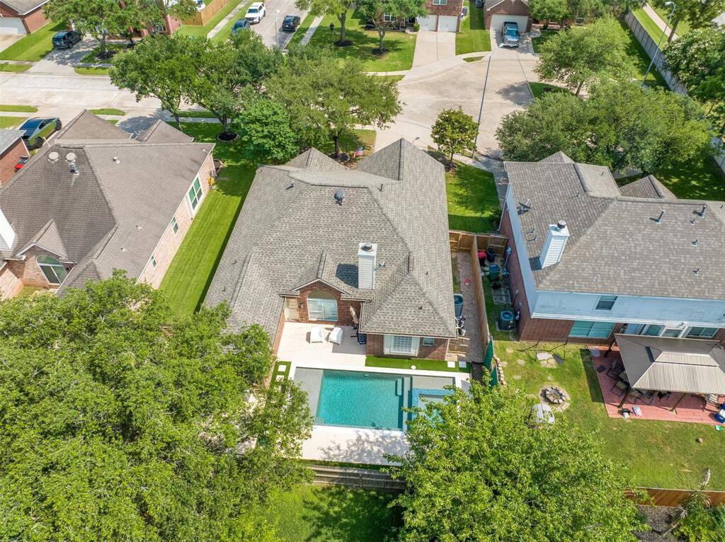This aerial view showcases a suburban home with a spacious backyard featuring a swimming pool and patio area. The property is surrounded by well-maintained lawns and neighboring houses, set in a quiet residential neighborhood with tree-lined streets.