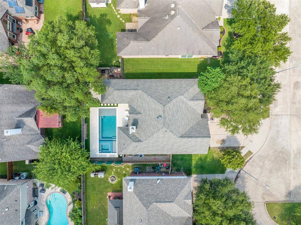 This aerial view showcases a suburban home with a spacious backyard featuring a pool. The property is well-maintained, with lush green lawns and mature trees providing privacy. It's situated in a quiet neighborhood with nearby houses, offering a comfortable and inviting setting.