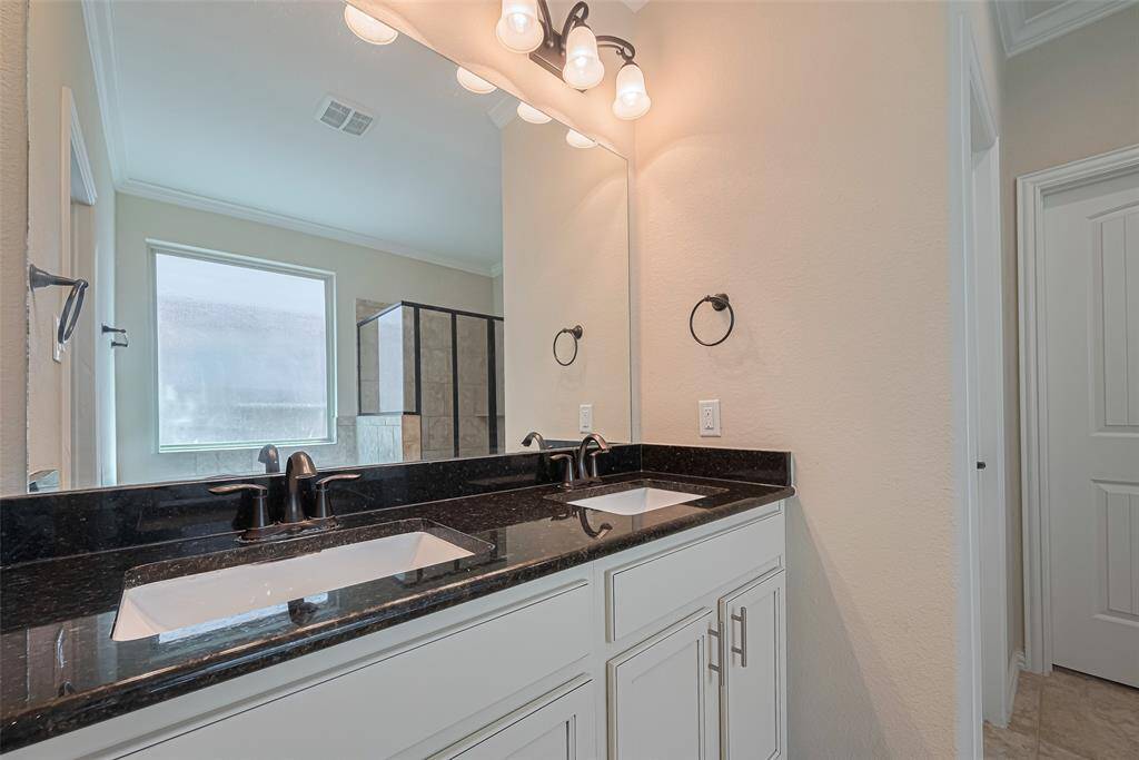 The stylish dual-sink vanity with white cabinetry is topped with a sleek black counter, tying in perfectly with the bathroom’s polished look.