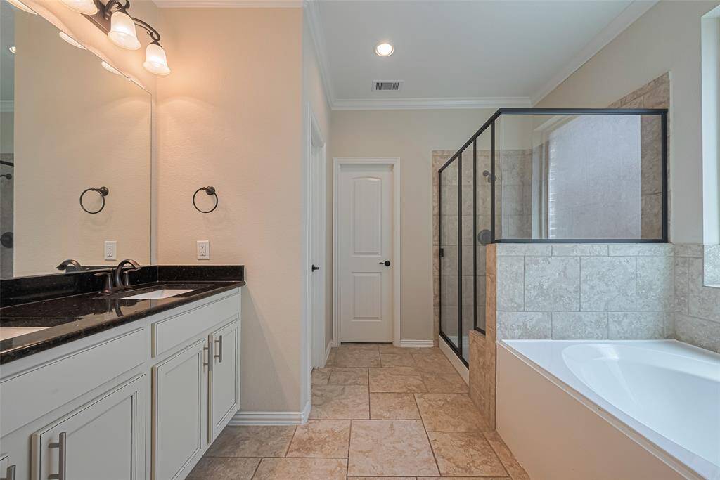 This spacious bathroom offers both form and function, featuring a soaking tub, glass-enclosed shower, and elegant vanity.
