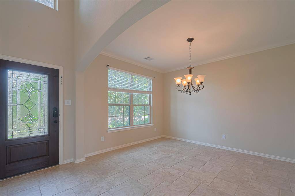Daylight pours through the oversized window, reflecting off the chandelier to create a glowing centerpiece in this refined dining space, perfectly framed by a broad archway.