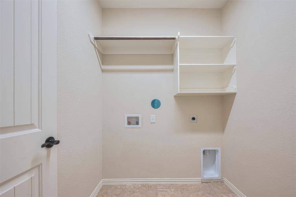 A functional laundry room with space to spare—featuring overhead shelving for storage and plenty of room for full-size appliances.