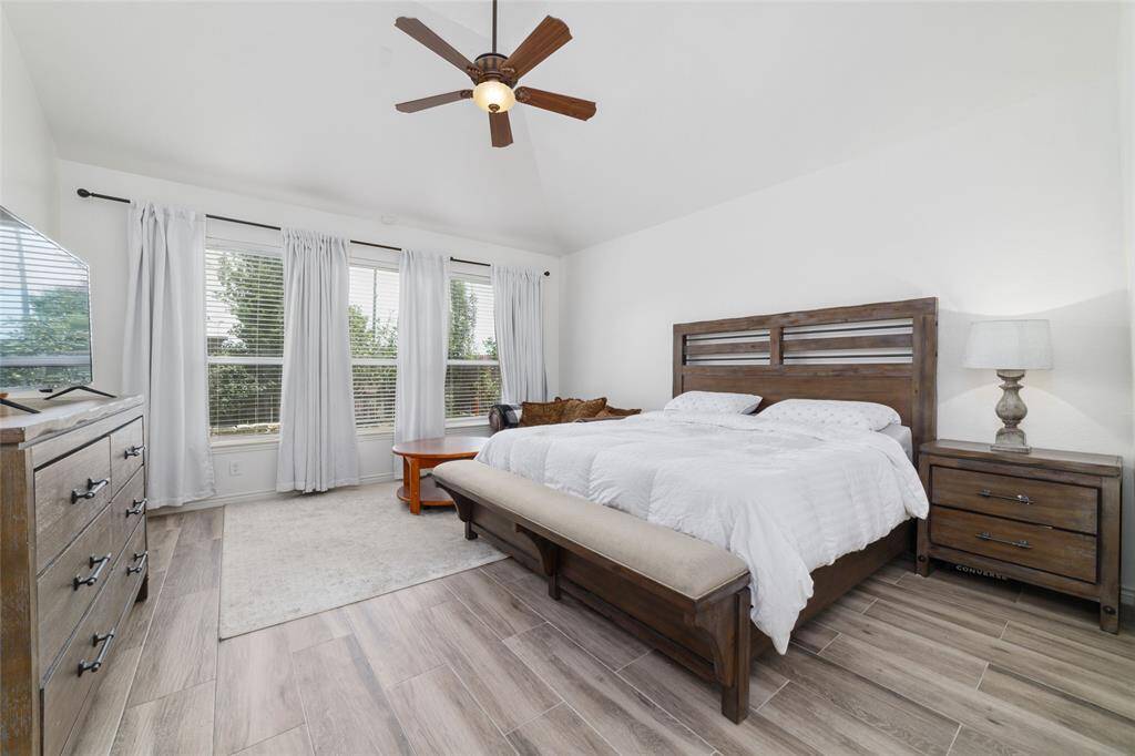 Spacious primary suite offers high ceiling with ceiling fan, wall of windows open to the backyard.