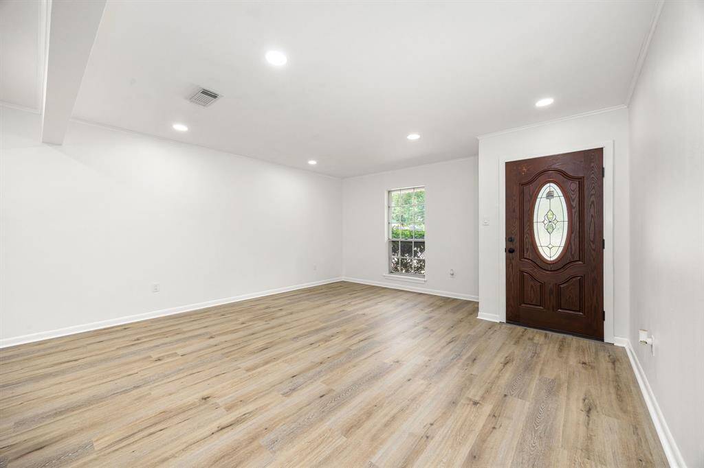 This room features a spacious, bright layout with fresh white walls and wood-look flooring. The large window allows for natural light, and the decorative wooden front door adds an elegant touch. Perfect for a welcoming entryway or living space.