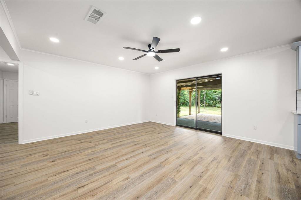 This spacious, bright living area features wood-style flooring, recessed lighting, and a ceiling fan. It opens to a backyard through large sliding glass doors, providing a seamless indoor-outdoor flow.