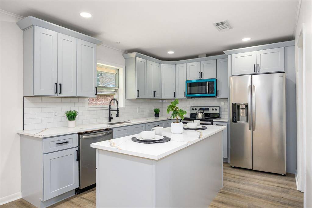 Modern kitchen with sleek grey cabinets, white subway tile backsplash, and stainless steel appliances. Features an island with seating and wood flooring for a warm, inviting atmosphere.