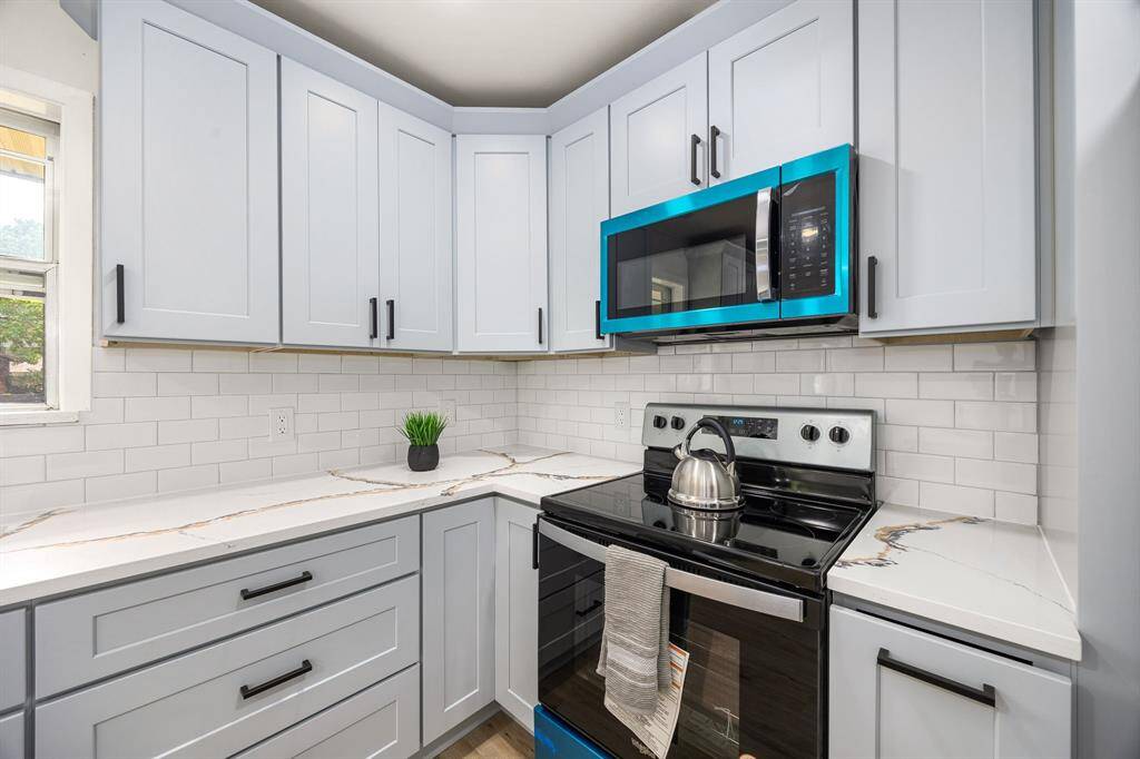 Modern kitchen with sleek white cabinetry, stylish black hardware, and a marble-look countertop. Features stainless steel appliances, including an electric stove and microwave. Subway tile backsplash adds a classic touch. Bright and inviting space.