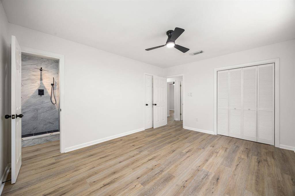 Spacious, bright bedroom with modern hardwood flooring and a ceiling fan. Features a walk-in closet and an en-suite bathroom with stylish marble accents.