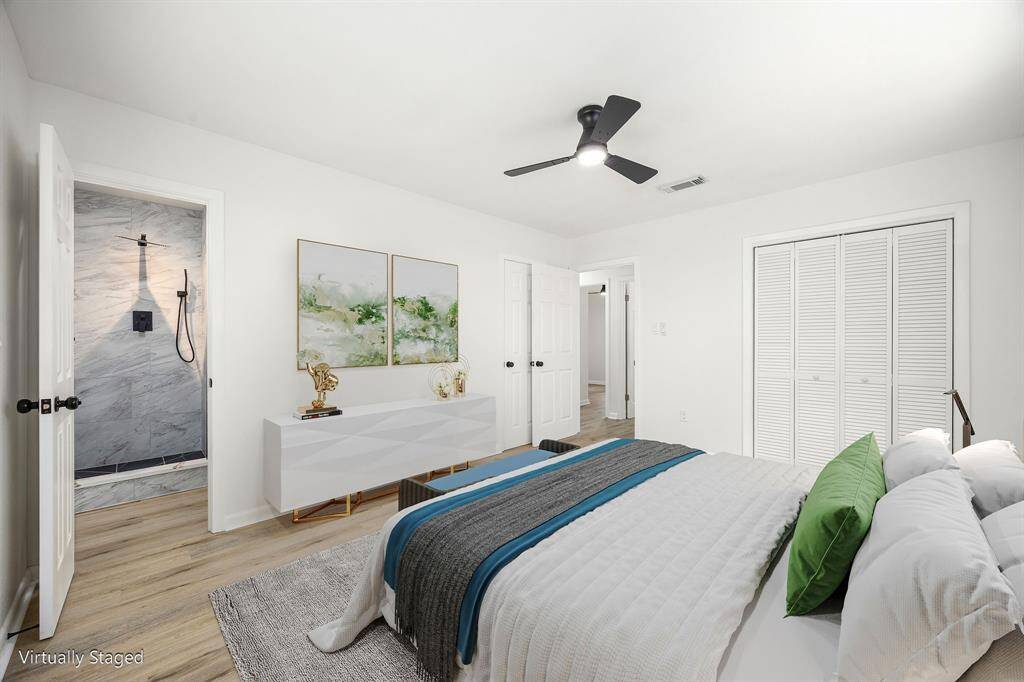 This is a bright, modern bedroom featuring a ceiling fan, stylish décor, and hardwood flooring. It has a sleek en-suite bathroom with a contemporary shower and ample closet space.
