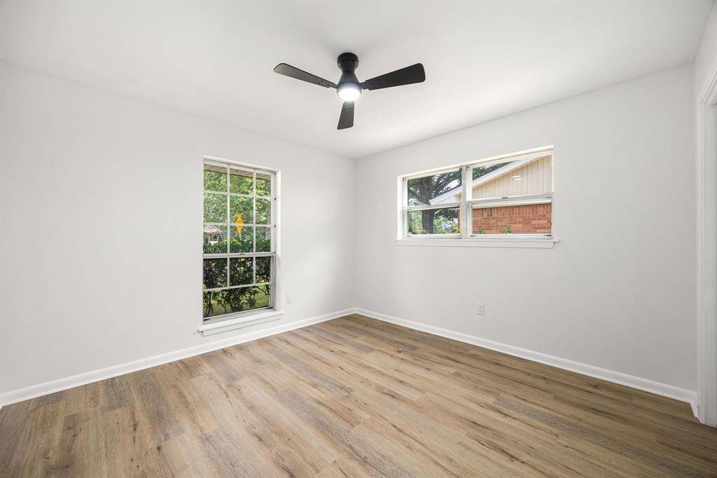 Bright, airy room with light wood flooring, two large windows for natural light, and a modern ceiling fan. Ideal for a cozy living space or bedroom.