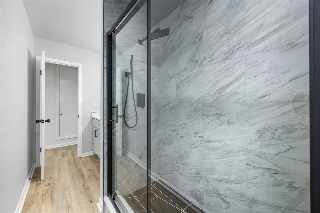 This bathroom features a modern glass-enclosed shower with elegant marble-like tiles, a sleek black showerhead, and light wood flooring, creating a clean and contemporary look.
