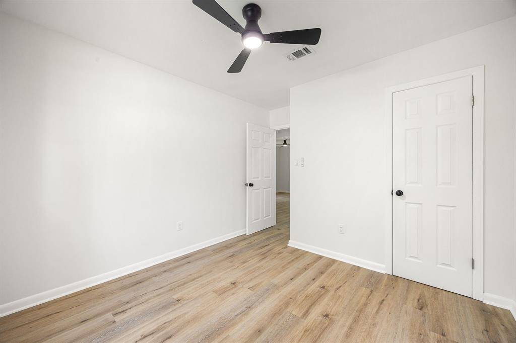 This room features fresh white walls, light wood flooring, and a modern ceiling fan. It offers two doors, adding convenience and accessibility.