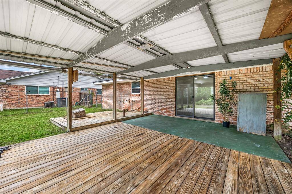 This photo showcases a spacious covered patio with wooden decking, ideal for outdoor gatherings. The area features a sliding glass door leading into the house and overlooks a grassy backyard, offering a serene extension of living space.