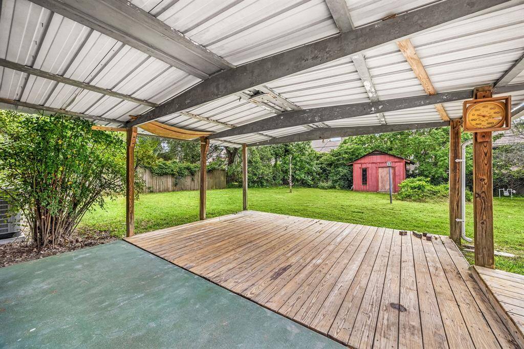 This photo showcases a covered wooden patio overlooking a spacious backyard with lush greenery and a charming red shed, ideal for outdoor relaxation and activities.
