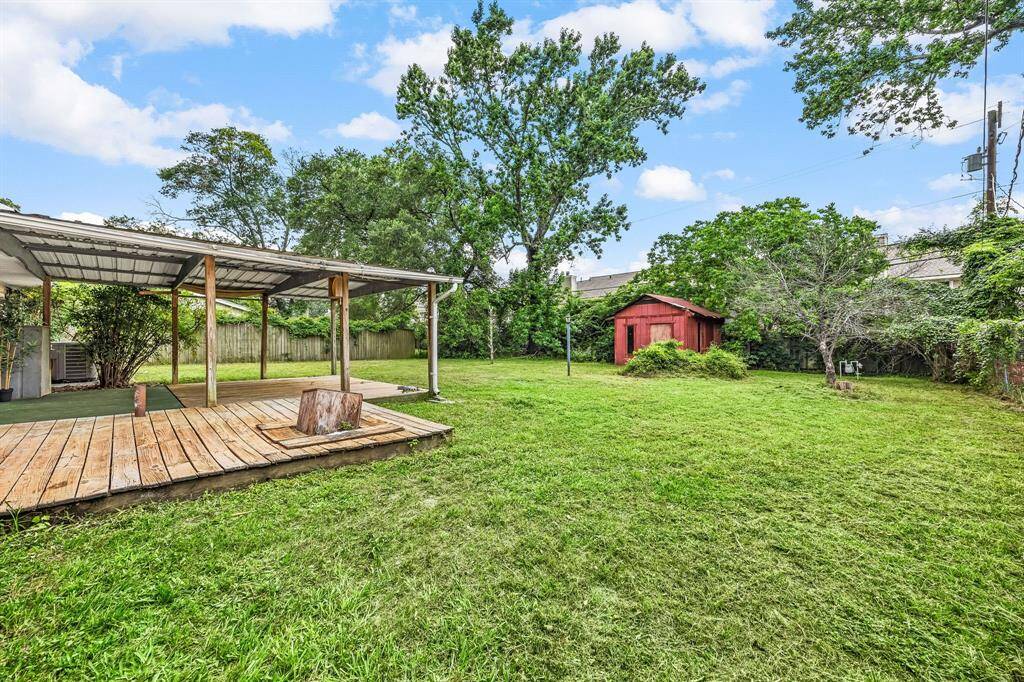 Spacious backyard featuring a covered patio with wooden decking, lush green lawn, mature trees, and a charming red storage shed. Perfect for outdoor activities and relaxation.
