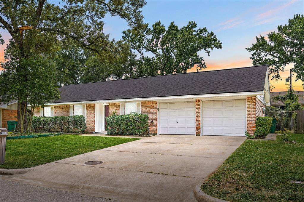 This charming single-story brick home features a spacious driveway leading to a two-car garage. The front yard is well-maintained with lush grass and mature trees, providing a welcoming curb appeal.