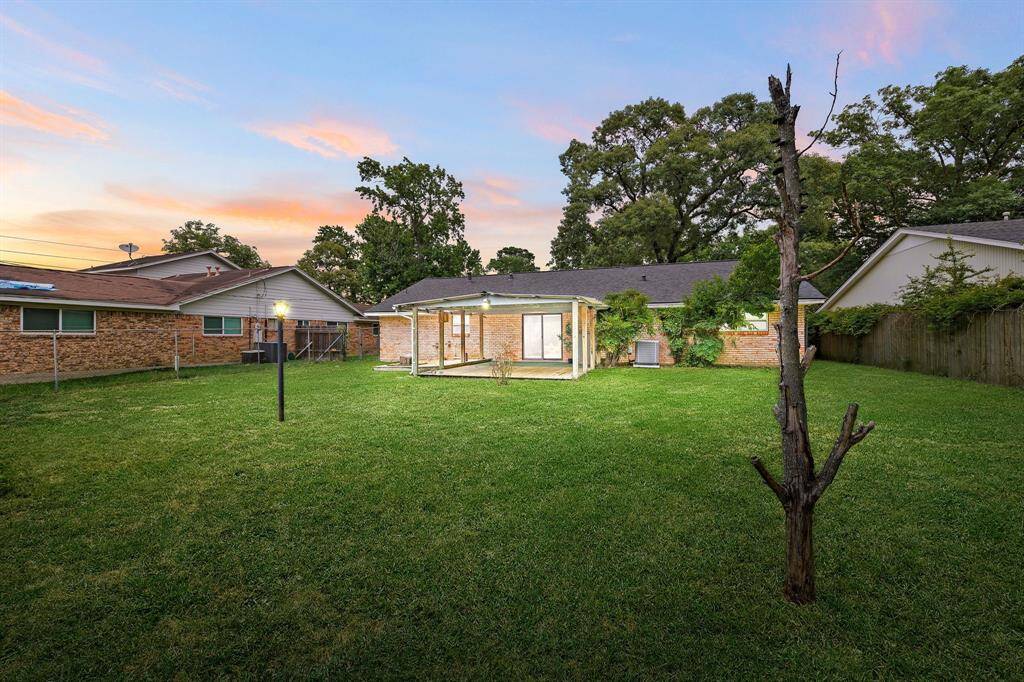 Spacious backyard with lush grass, ideal for outdoor activities. The house has a covered patio area, perfect for relaxing or entertaining. Surrounded by mature trees, providing privacy and a serene atmosphere.