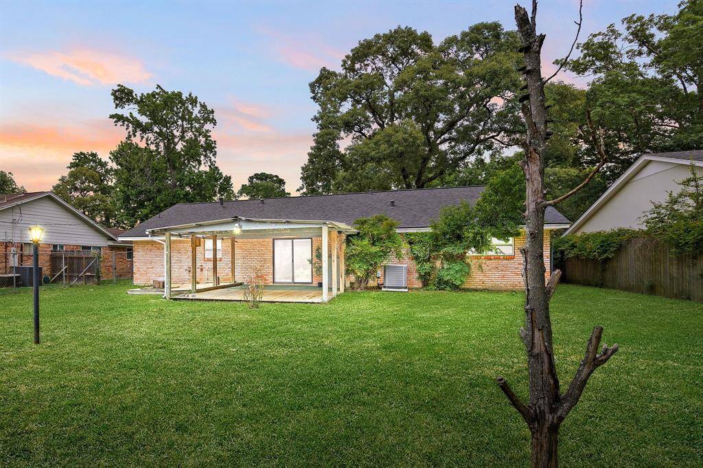 This photo showcases a spacious backyard with a well-maintained lawn, a covered patio attached to a single-story brick house, and mature trees providing privacy and shade.