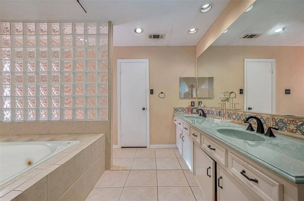 Enjoy a spa-like experience with dual vanities, glass block detail, and a large soaking tub—your personal escape at home.