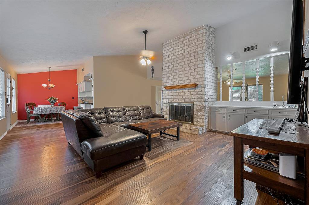 Vaulted ceilings, warm wood floors, and a statement brick fireplace create a cozy yet open space, seamlessly flowing into a cheerful dining nook.