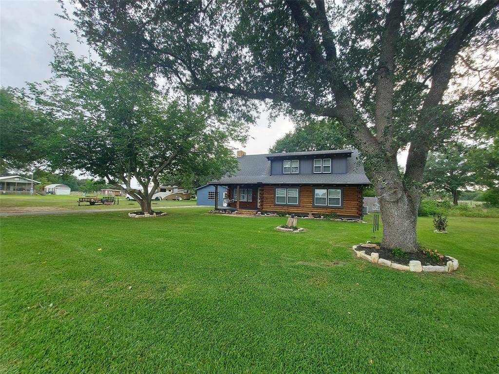 Charming two-story home with rustic wood siding set on a spacious, well-maintained lawn. The property features mature trees and a welcoming front porch, offering a serene and inviting atmosphere.
