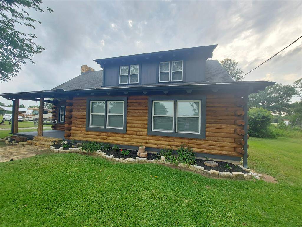This charming log cabin-style home features a cozy porch and a well-maintained lawn with stone-bordered landscaping. The exterior showcases wood siding and a dark roof, offering rustic appeal in a peaceful setting.