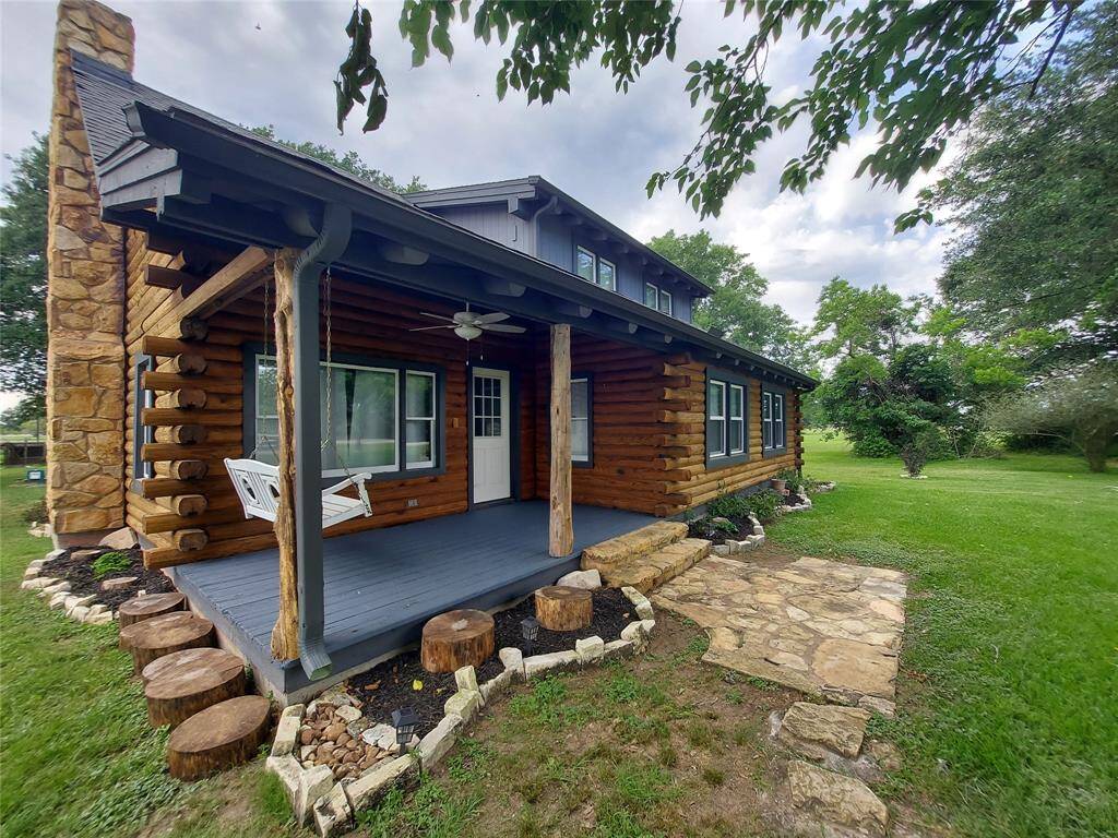 This charming log cabin features a cozy front porch with a swing, rustic stone accents, and a well-maintained lawn surrounded by mature trees, offering a perfect blend of comfort and nature.