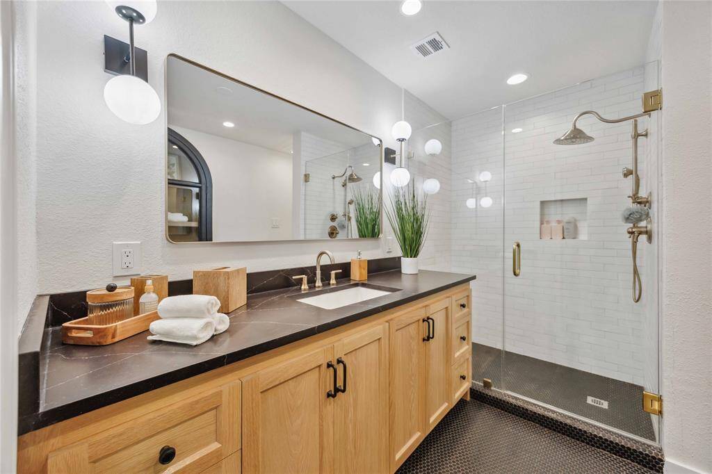 A 1st-floor full bath features a frameless glass shower with custom tiles from Cle Tile. Elegant light fixtures, a granite countertop, and white oak cabinetry accent premium fixtures to showcase this spa-like bath.