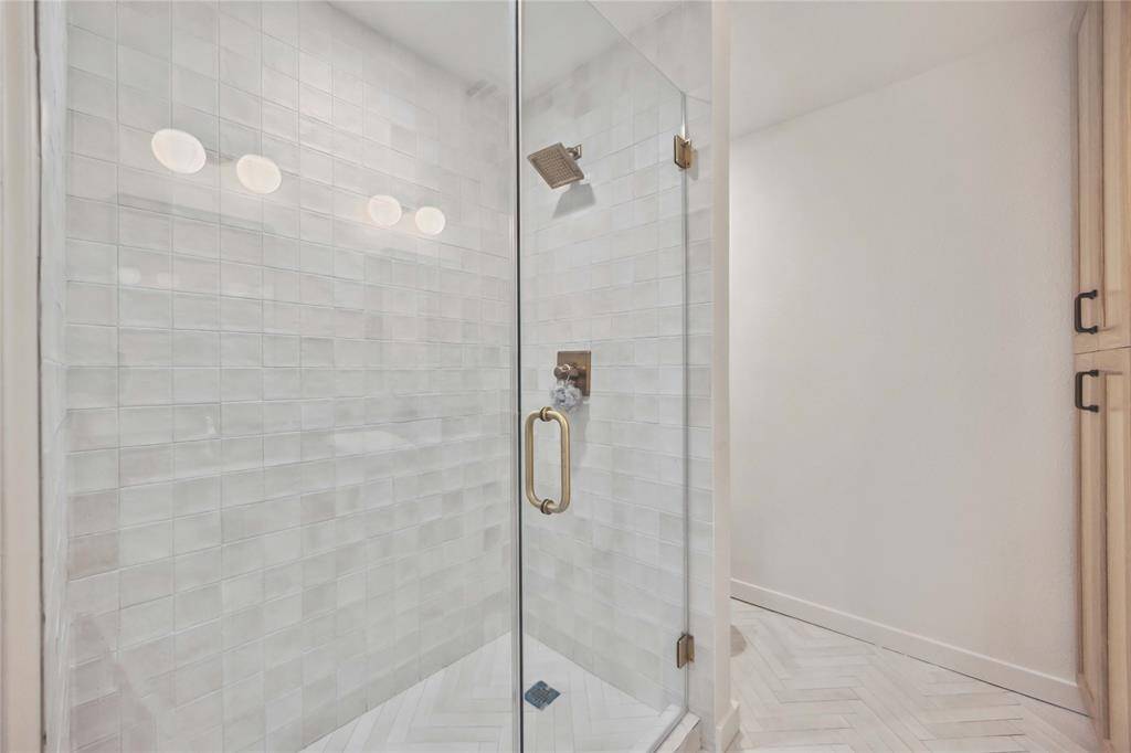 A stylish frameless glass shower in the primary bath offers a better view of the custom shower tiles seen in the other bathrooms.