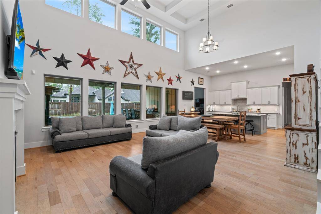 This is a spacious, open-concept living and dining area with high ceilings, ample natural light, a modern kitchen with white cabinetry, and hardwood floors. The room features a view to the backyard.