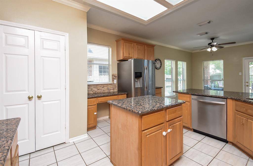 This kitchen features granite countertops, a central island, stainless steel appliances, and ample wooden cabinetry. The bright, open feel, with mosaic backsplash and stainless appliances add a stylish touch.