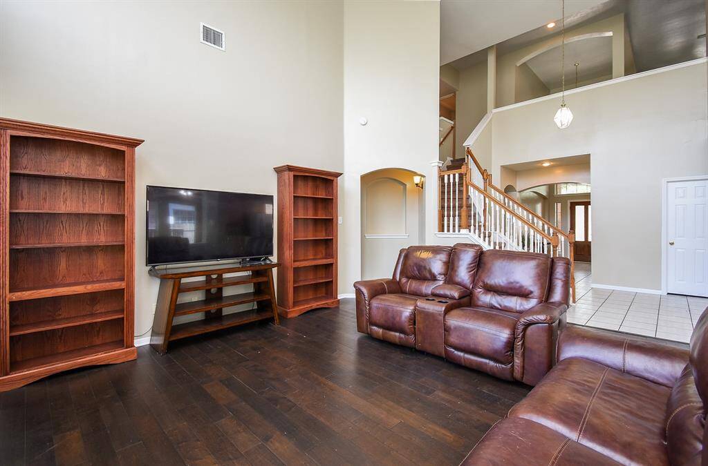 This spacious living room features high ceilings, abundant natural light from large windows, and a cozy fireplace. It flows into an open dining area, creating a welcoming space for entertaining.