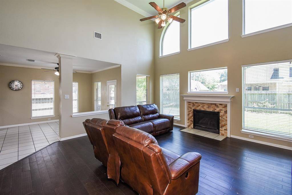 This spacious living room features high ceilings, large windows for natural light, a cozy fireplace, and elegant hardwood floors.