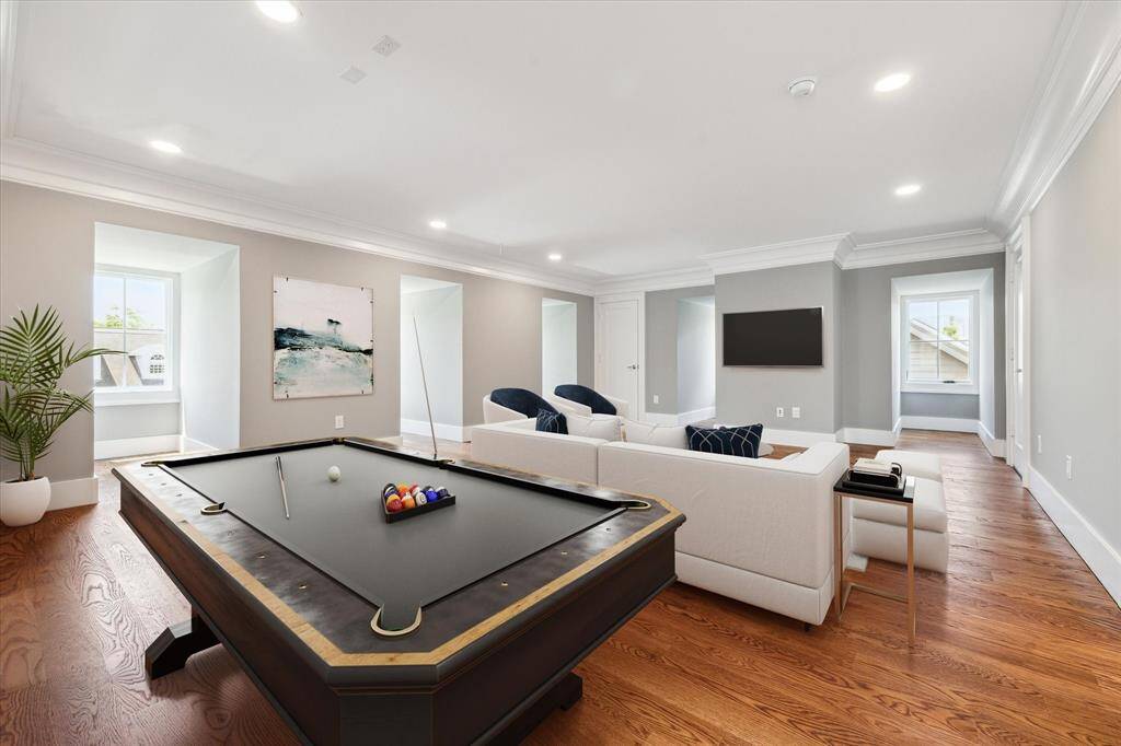 This 3rd floor flex/media/game room is a spacious, well-lit living area features elegant hardwood floors, a cozy seating arrangement, and a stylish pool table. Large windows bring in natural light, while modern decor and a minimalist design create a welcoming atmosphere.  Use your own imagination for what your family would like here!  This photo has been virtually staged.