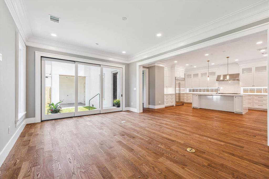 This photo showcases a spacious open-concept living area with hardwood floors, large sliding glass doors leading to the outdoor space, and a modern kitchen featuring an island and ample cabinetry. The area is well-lit with recessed lighting and pendant lights above the island.