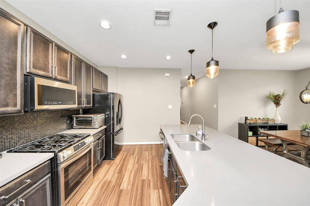 This stunning kitchen displays such abeautiful contrast with the darkstained cabinets, neutral paint,light countertops, dark modernbacksplash, and SS appliances.