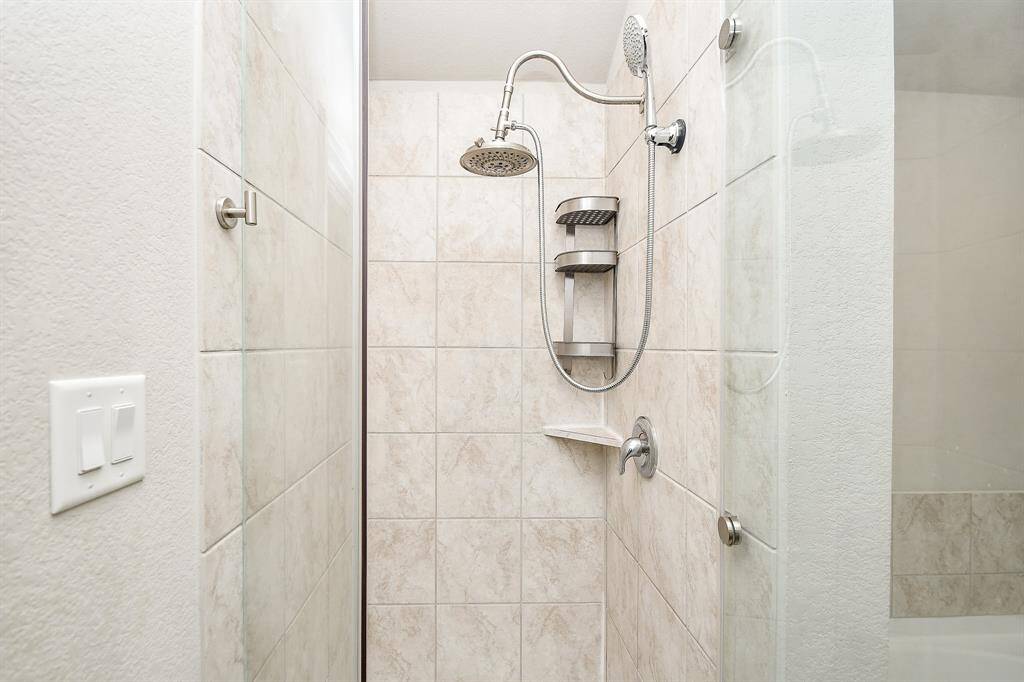 Warm earth toned tile surround comforts you in the primary walk-in, glass enclosed shower.
