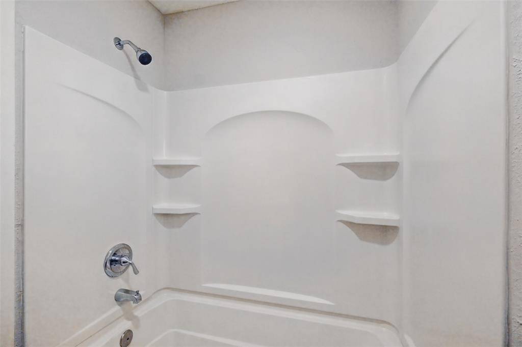 This photo shows a clean, white bathtub and shower combo with built-in shelving for storage.