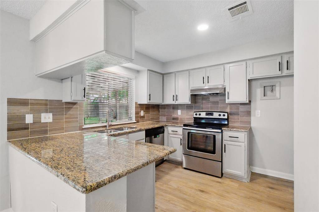 This modern kitchen features granite countertops, stylish tile backsplash and gray cabinetry with attractive hardware.