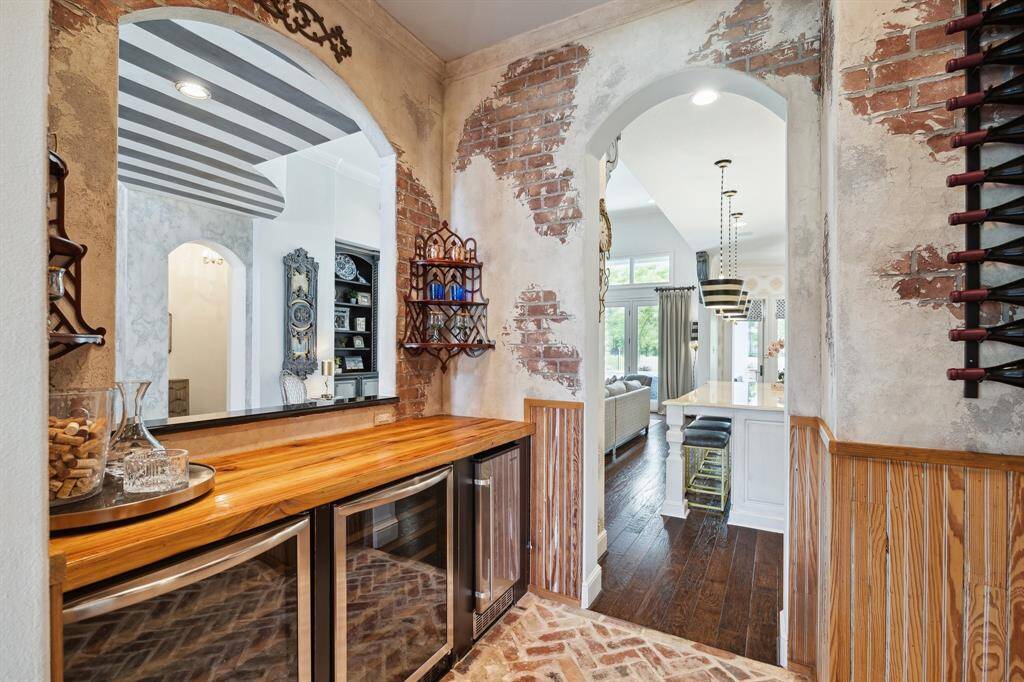 A charming wine room provides a transition between the formal dining room and the chef's kitchen. A interior window open to the formal entry allows for effortless serving and entertaining. This grotto features storage cabinetry, two wine coolers that can chill up to 116 bottles and an ice maker. Reclaimed Louisiana pine adorns the walls and countertops.