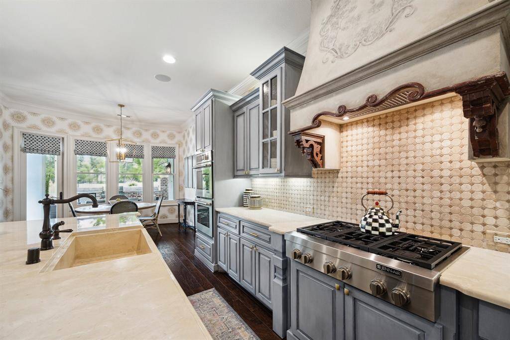 The details of the custom designed oversized vent hood, classic subtle pattern in the natural stone backsplash as well as the sophisticated color palette of the cabinetry is evident in this view.