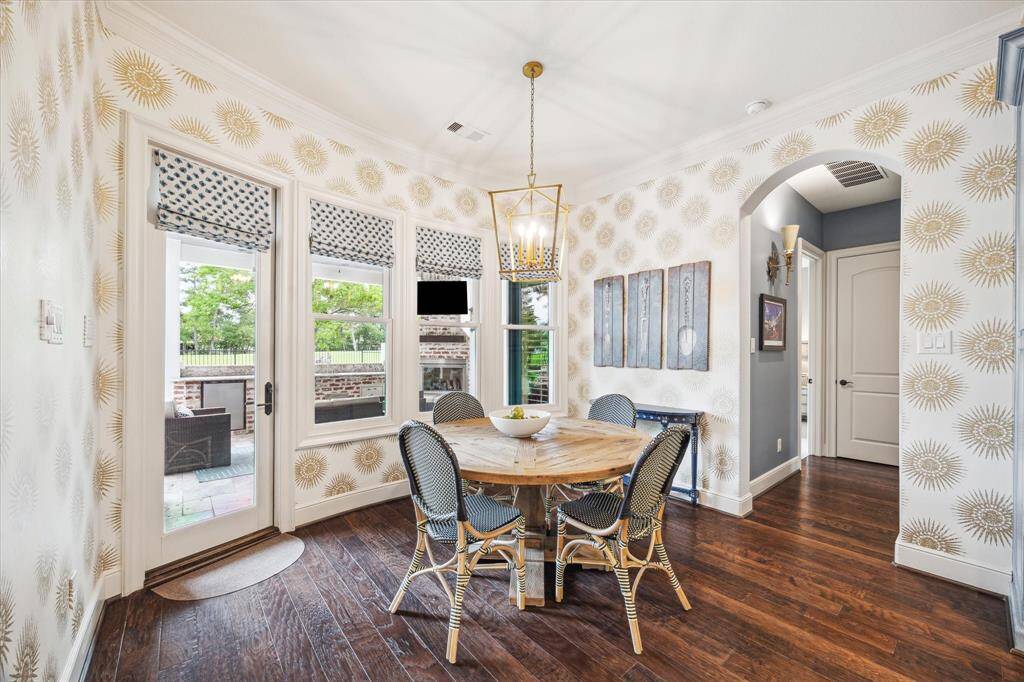 The kitchen and breakfast area walls are covered in a metallic and linen wallpaper by Thibault with striking sunburst medallions. A brass pendant, custom Roman shades and the illuminating natural light from the windows combine with the wallpaper to boldly reflect the unique personality of the show-stopping space.